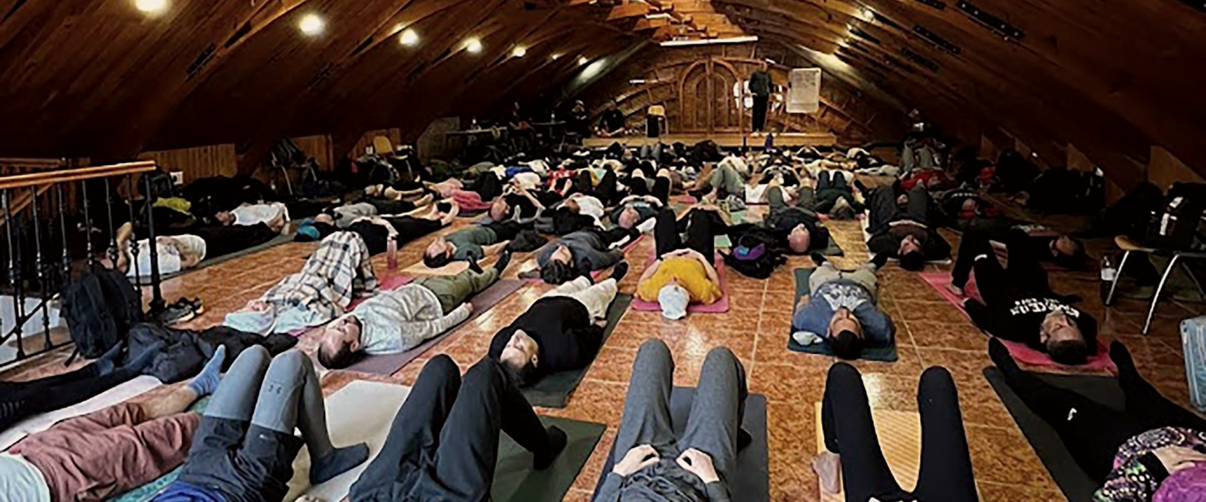Groep ligt op matten tijdens een ademwerksessie in een houten zaal